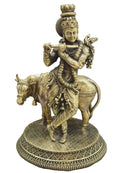 An antique brass statue of Lord Krishna riding a cow, set against a neutral gray background.