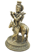 An antique-style brass statue of Lord Krishna playing a flute , mounted on a circular decorative base.